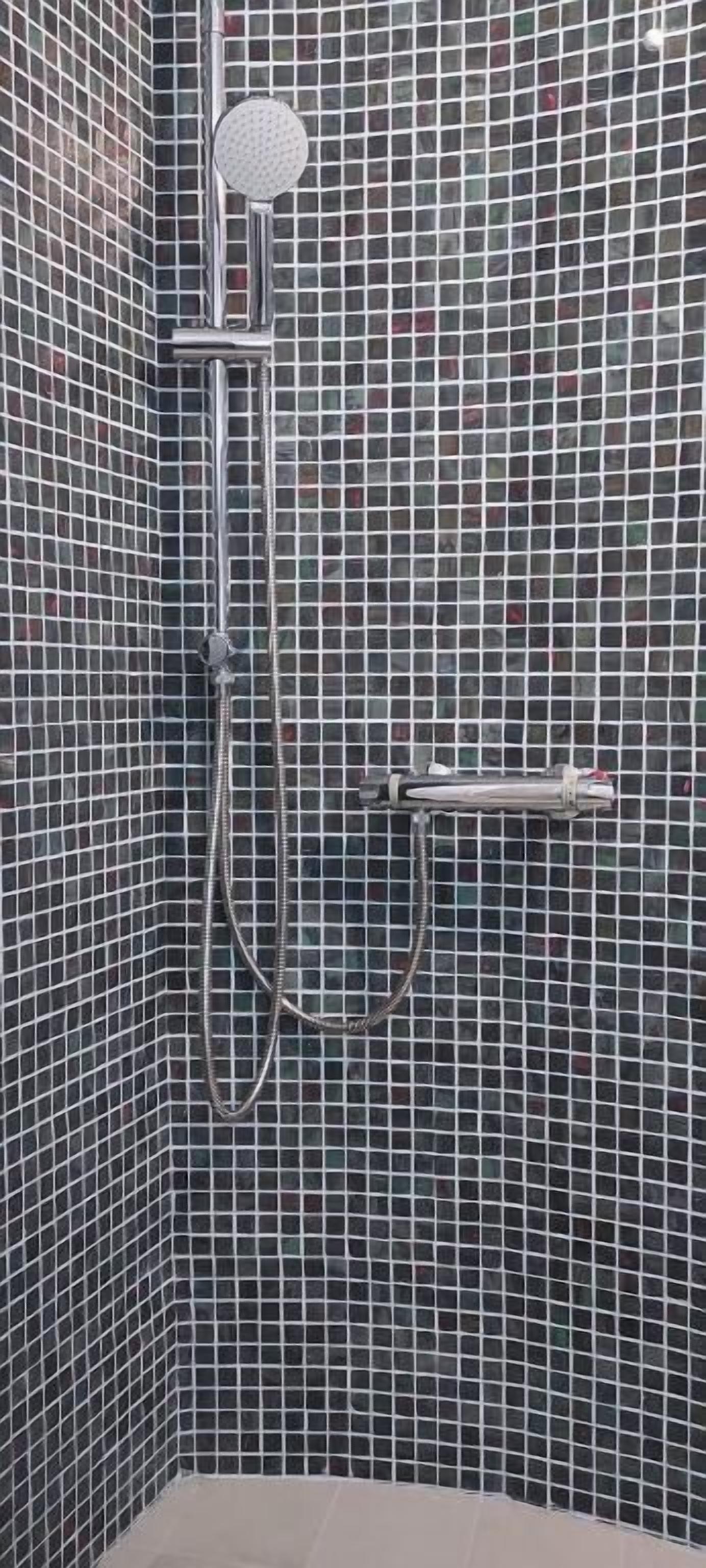 A shower area with a handheld showerhead and a wall-mounted faucet.