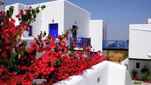 A white building with blue accents, a balcony, and red flowers in the foreground. - Aegeo Hotel (Folegandros)