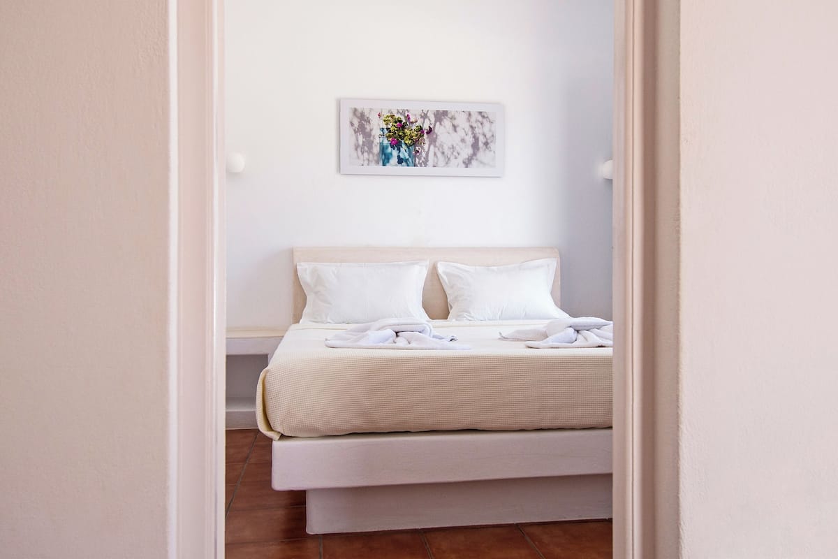 A bedroom with a bed, white pillows, a white headboard, and a wall-mounted artwork.