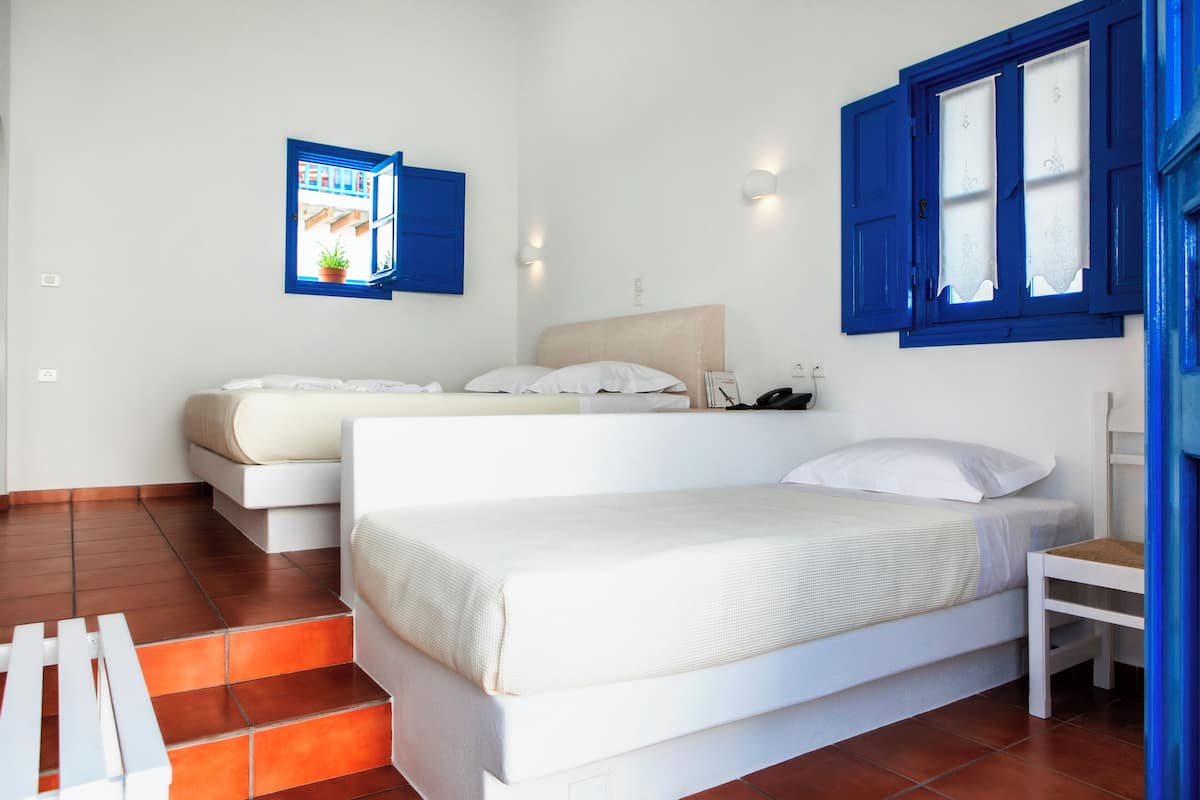 A bedroom with two beds, a small table, and a window with blue shutters.