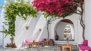 An outdoor seating area with stone flooring, wooden furniture, and potted plants. - Aegeo Hotel (Folegandros)