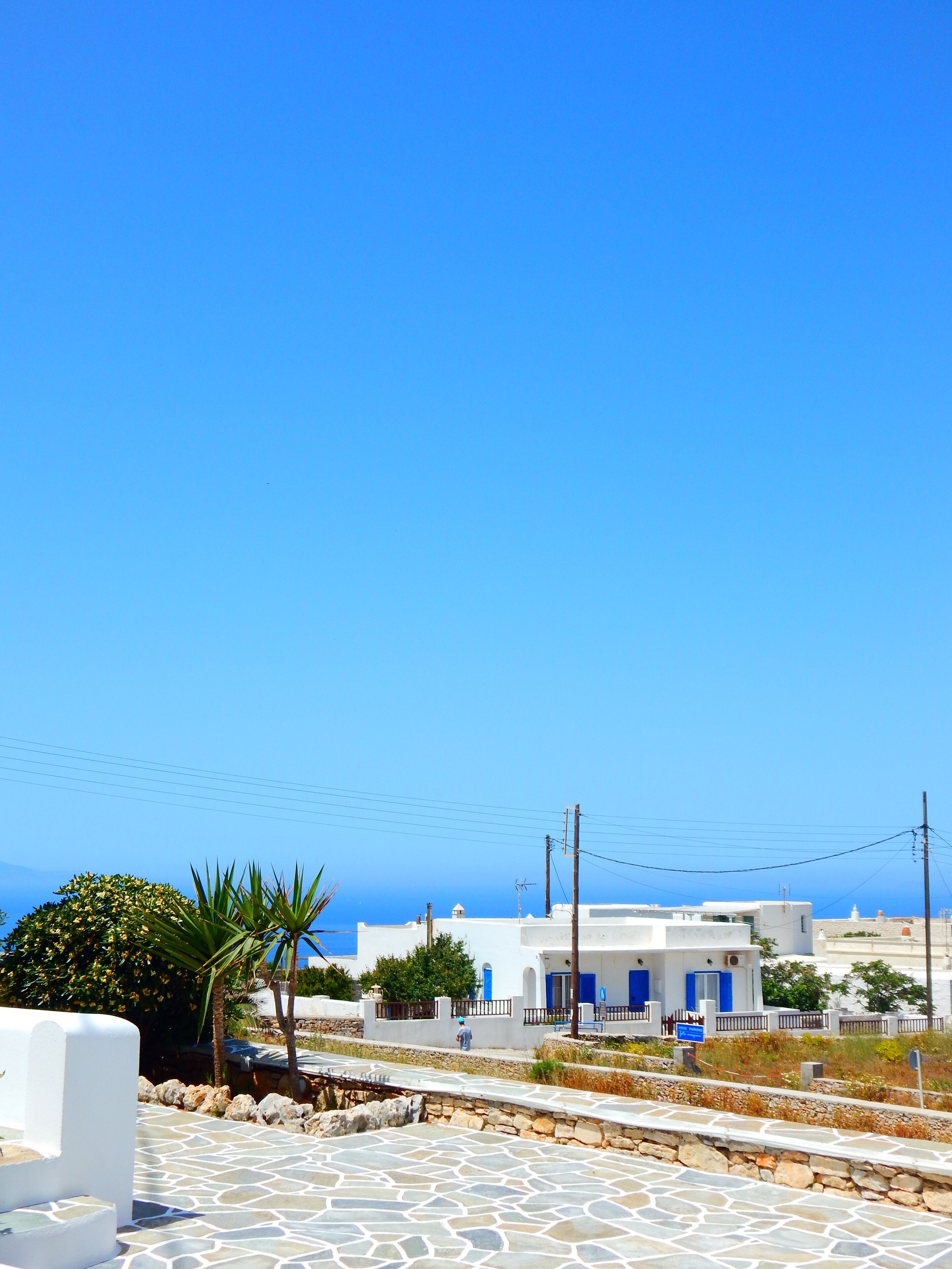 A coastal town with white buildings, a stone-paved area, and a clear blue sky.