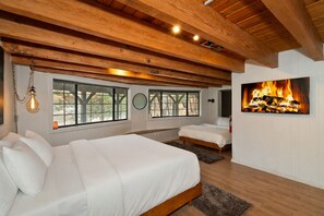 Ein Schlafzimmer mit zwei Betten, Holzbalken, großen Fenstern und einem Kamin.