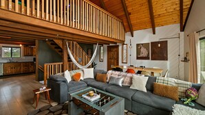 A spacious living area with a large sofa, a coffee table, and a wooden ceiling. - Walk to Bear Mountain Slopes! Hot Tub Game Room! Fire Pit! Super cute! (Big Bear Lake)