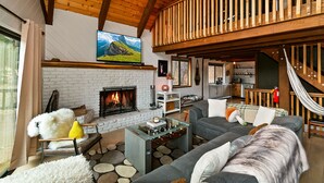 A cozy living room with a fireplace, a sofa, a coffee table, and a hammock. - Walk to Bear Mountain Slopes! Hot Tub Game Room! Fire Pit! Super cute! (Big Bear Lake)
