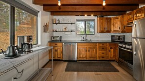 A modern kitchen with wooden cabinets, stainless steel appliances, and a large window. - Walk to Bear Mountain Slopes! Hot Tub Game Room! Fire Pit! Super cute! (Big Bear Lake)