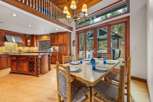 A spacious kitchen with wooden cabinets, a large island, and a dining area with a wooden table and chairs. - Private Hot Tub, Game Room, 3,450 sq ft, Beautiful Home! Close to Everything (Big Bear City)