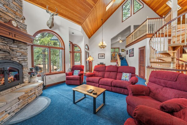 A spacious living room with a stone fireplace, red sofas, and a wooden staircase. - Private Hot Tub, Game Room, 3,450 sq ft, Beautiful Home! Close to Everything (Big Bear City)