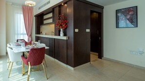 A modern kitchen with a built-in island, a dining area with a white table and red chairs, and a painting on the wall. - ina Homes - 1 BHK Tower 5 (Dubai)