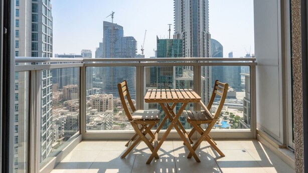 A balcony with a table and chairs, offering a view of a cityscape with tall buildings. - ina Homes - 1 BHK Tower 5 (Dubai)