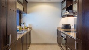 A narrow kitchen with wooden cabinets, a microwave, and a sink. - ina Homes - 1 BHK Tower 5 (Dubai)