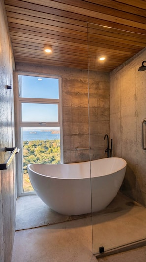 Ein modernes Badezimmer mit einer freistehenden Badewanne, einer Dusche und einem großen Fenster mit weitem Panoramablick.