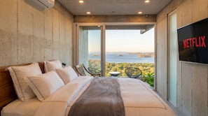 Ein Schlafzimmer mit einem großen Bett, einem an der Wand befestigten Fernseher und einem Balkon mit Meerblick.