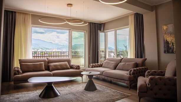 Un salón amplio con un conjunto de sofás modernos, una mesa de centro y grandes ventanales con vistas a la ciudad y las montañas.