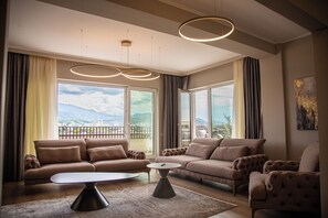 Un soggiorno spazioso con un divano moderno, un tavolino da caffè e ampie finestre che offrono vista sulla città e sulle montagne.