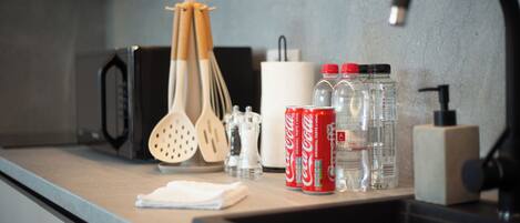 A kitchen counter with a microwave, wooden utensils, a white paper towel holder, and two Coca-Cola cans.
