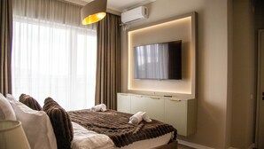 Una habitación de hotel moderna con una cama grande, un televisor de pantalla plana montado en la pared y un aire acondicionado instalado en el techo.