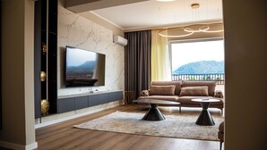 Una sala de estar moderna con un televisor de pantalla plana montado en una pared de mármol, un sofá, una mesa de centro y vistas a montañas a través de un ventanal grande.