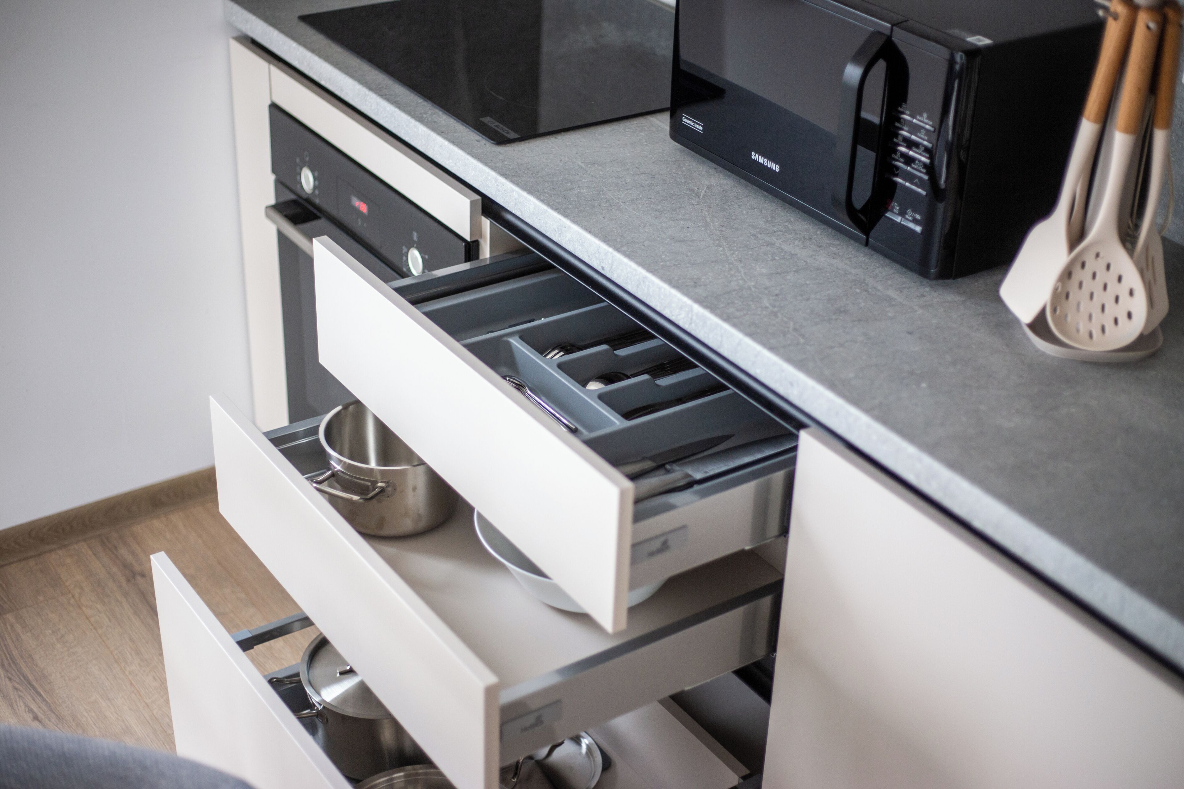 A kitchen with a microwave, a stainless steel pot, and a drawer with a metal pot inside.