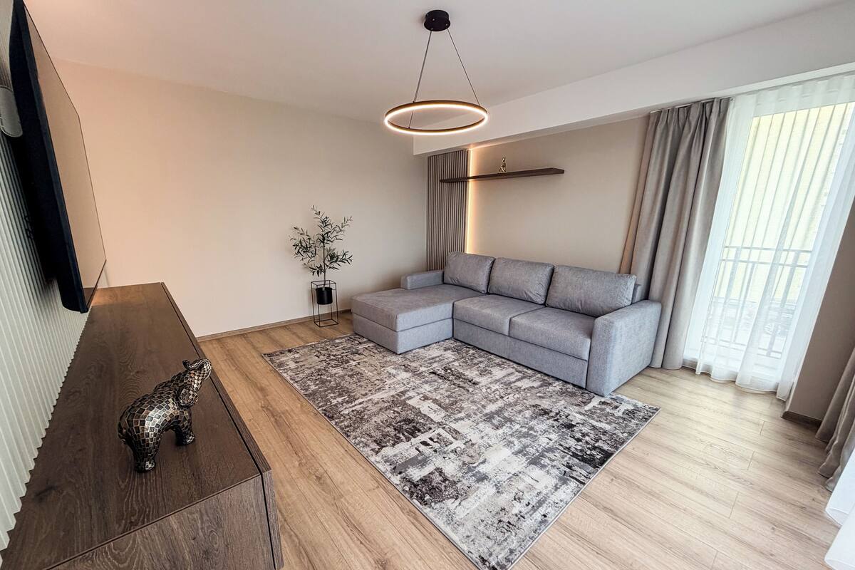 Un salon moderne avec un canapé d’angle, une table basse en bois, un tapis à motifs et un luminaire suspendu.