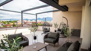 Un balcón amplio con vistas a la ciudad y a las montañas, amoblado con un sofá, sillas y una mesa.