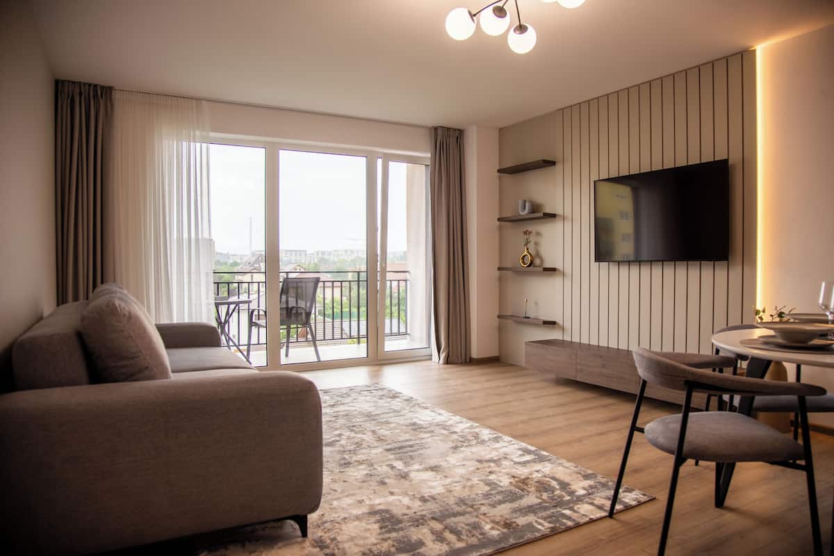 Un salon moderne comprenant un canapé, une table à manger avec des chaises, un téléviseur à écran plat fixé au mur et un balcon avec vue.