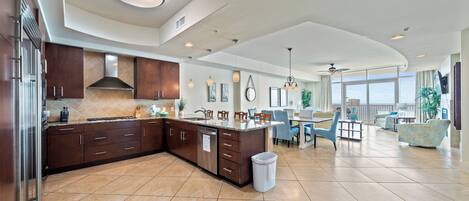 A spacious kitchen with dark wooden cabinets, a large island, and a dining area with blue chairs and a table.