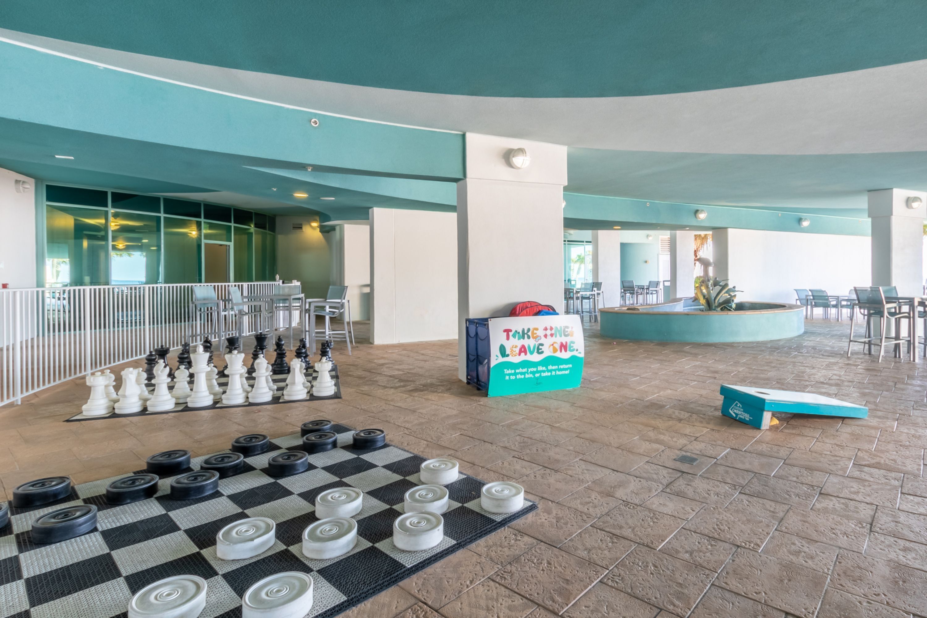 Un espacio interior amplio con un juego de mesa de piso a cuadros, arreglos de asientos y un cartel que promueve una política de no usar color beige.