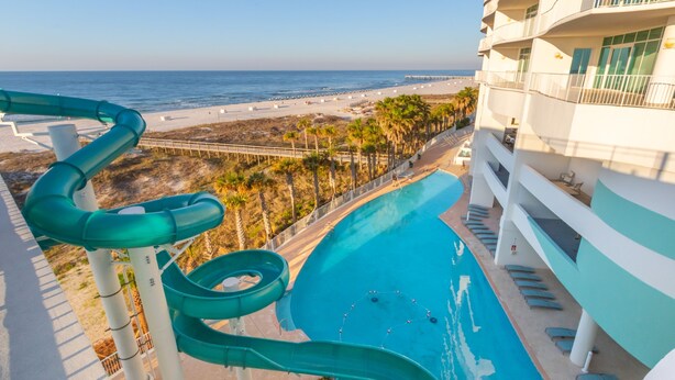 Tobogán que desemboca en una piscina con vista a la playa y al océano.