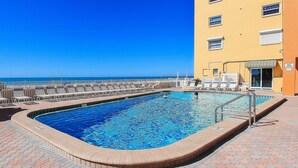 Uma piscina com vista para o oceano, rodeada por espreguiçadeiras e um edifício com várias janelas.