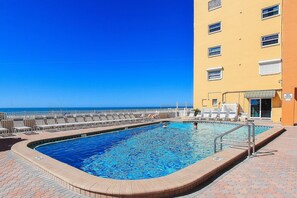 Ein Pool mit Meerblick, umgeben von Liegestühlen und einem Gebäude mit vielen Fenstern.