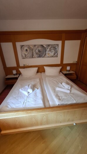 Ein Doppelbett mit weißen Leinen und Handtüchern, ein Holzkopfbrett, Nachttische mit Lampen und ein großes abstraktes Gemälde an der Wand.
