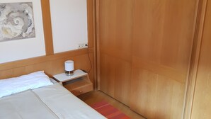 A bedroom with a bed, a nightstand, a power outlet, a wooden wardrobe, and a wall art piece.