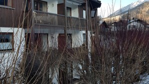 A two-story building with a balcony, wooden exterior, and a view of snow-covered mountains.