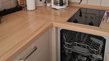 A kitchen with a coffee maker, a dishwasher, and a countertop with a cutting board and paper towel holder.