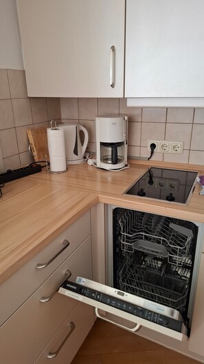 Een keuken met een koffiezetapparaat, een vaatwasser en een aanrecht met een snijplank en een keukenpapierhouder.