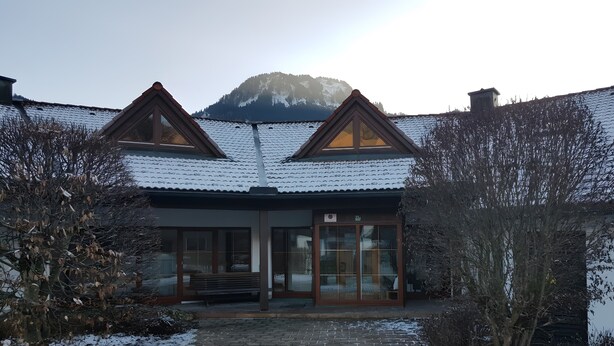 A building with a snow-covered roof, a wooden bench, and a paved entrance.