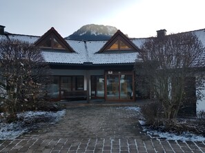 Un bâtiment dont le toit est recouvert de neige, avec un banc en bois et une entrée pavée.