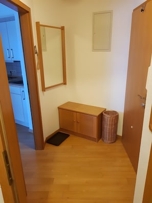 A hallway with a wooden cabinet, a small trash bin, and a door leading to a kitchen area. - Apartment 'Hindelanger Auszeit' with Mountain View, Balcony and Wi-Fi (Bad Hindelang)