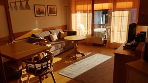 A living room with a sofa, dining table, chairs, a TV, and a radiator.