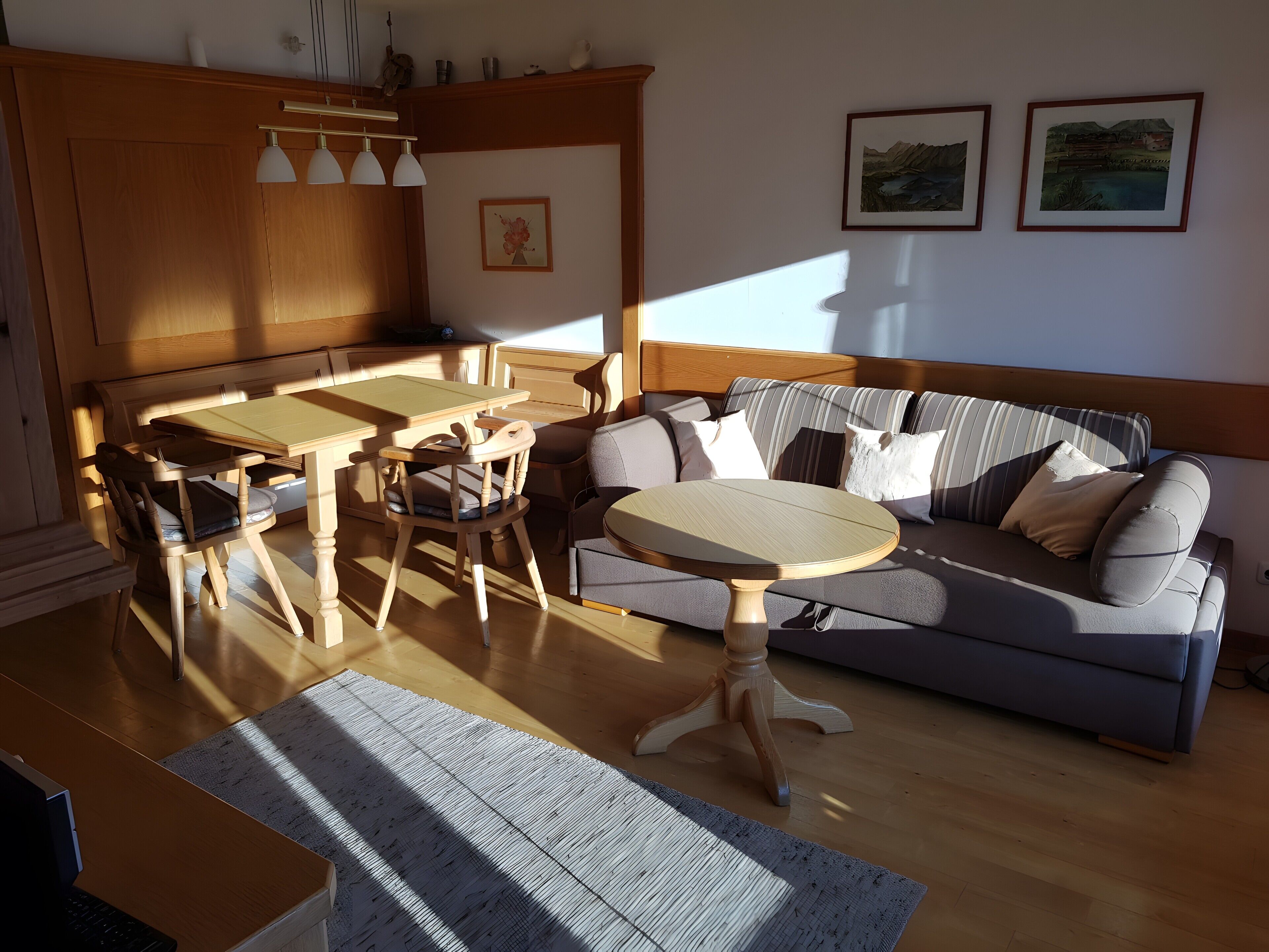 A living room with a wooden dining table, chairs, a sofa, and a coffee table. There are two framed pictures on the wall.