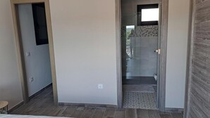 Een slaapkamer met een bed, een houten vloer en een glazen deur die leidt naar een badkamer met een betegelde douche.