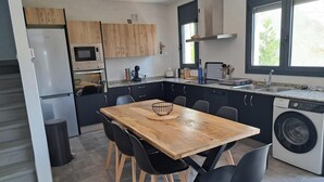 Een moderne keuken met een houten tafel, zwarte stoelen, een inbouwoven, een magnetron en een wasmachine.