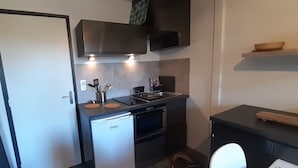A compact kitchen with a dishwasher, oven, and a microwave. There is a sink with a faucet and a countertop with a cutting board and utensils. - La Louvatière, in the heart of the village, the ideal place to discover the Monts Jura. (Mijoux)