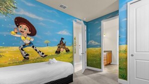 Un dormitorio con un mural de un personaje de dibujos animados, una cama y una puerta que da a otra habitación.
