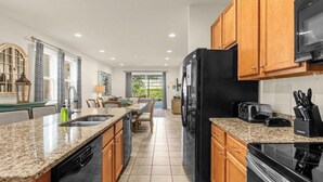 Una cocina con encimeras de granito, armarios de madera, un refrigerador negro y un microondas.