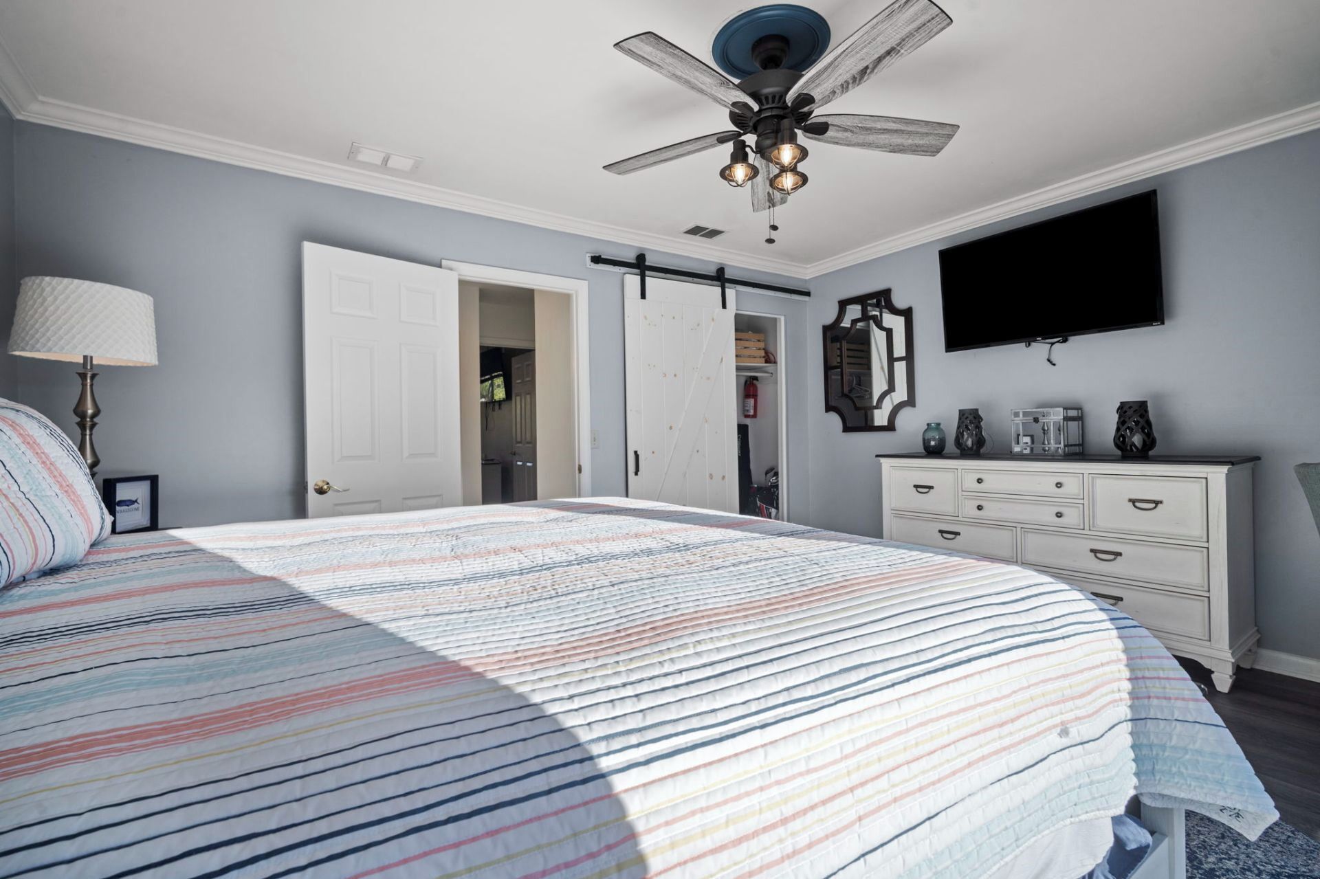 A bedroom with a bed, a ceiling fan, a dresser, and a TV mounted on the wall.