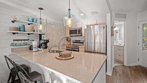Cozinha moderna com bancadas de granito, eletrodomésticos de aço inoxidável e iluminação pendente.