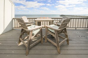 Une terrasse en bois avec deux chaises et une table, donnant sur une plage et une jetée.