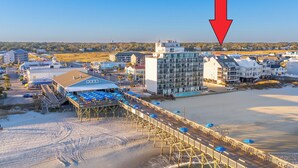 Ett hotell vid kusten med en träbrygga, utsikt över stranden och moderna byggnader.